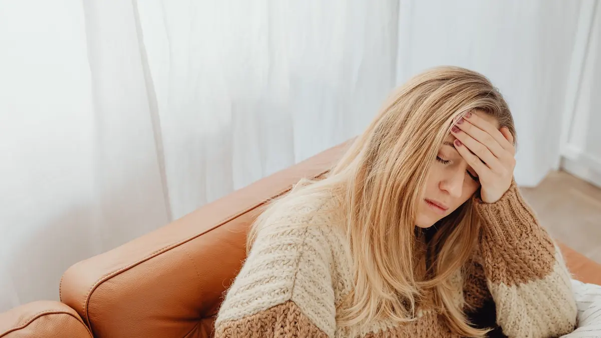 Woman sitting on a leather sofa with her hand on her forehead and her eyes closed