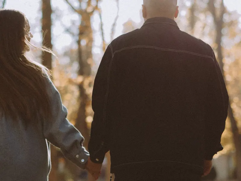 Two adults walking hand in hand among autumn trees, seen from behind