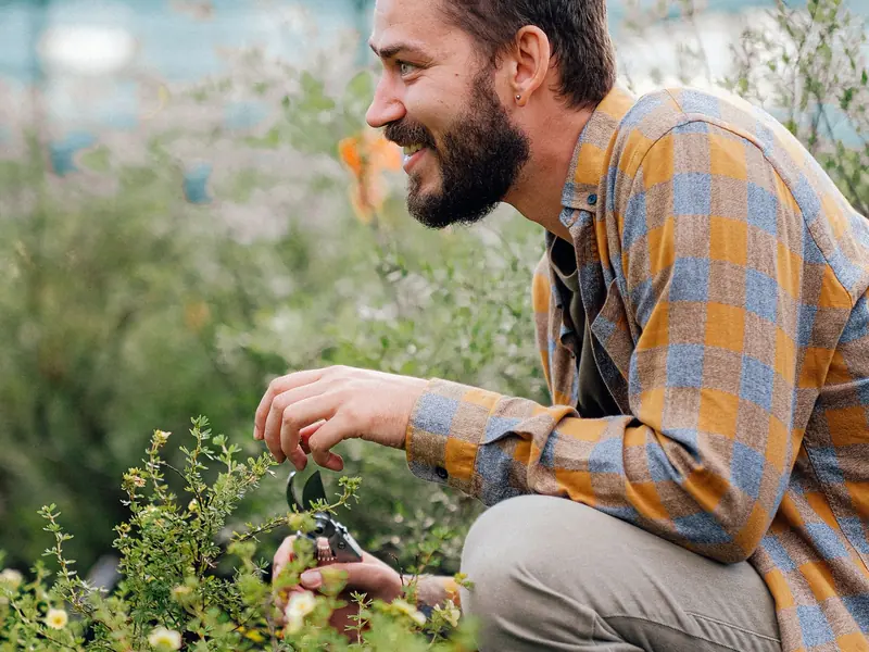 A smiling man crouching in a garden and tending plants
