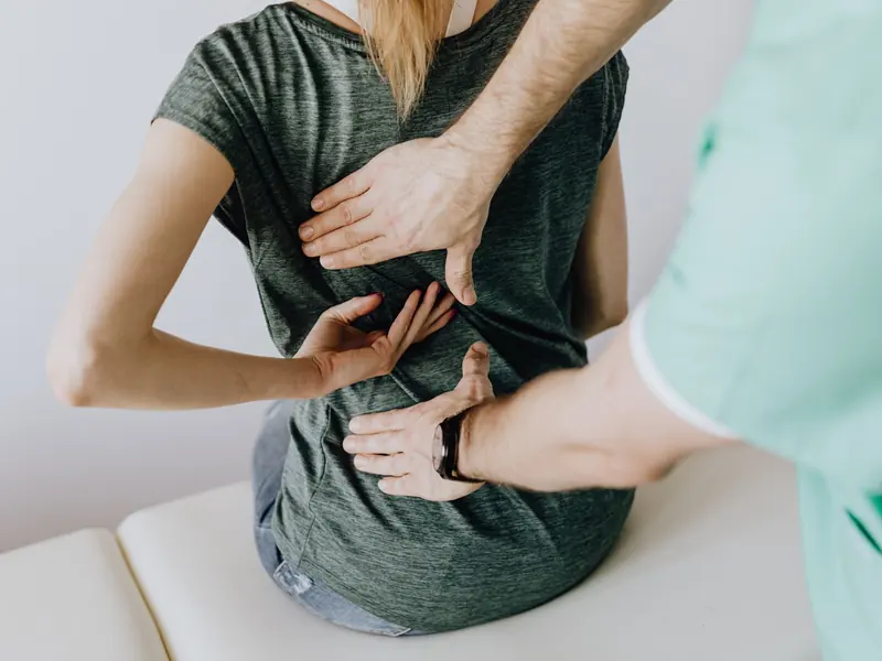 A clinician checking a seated woman's lower back with both hands